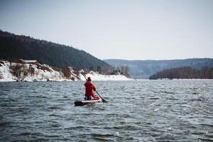 A SUP boarder paddles along a river against the background of mountains, a man sits on a board and travels on a mountain lake, a hiking trip in spring on Fode. photo