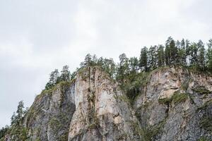 A mountainous outcrop covered in dense trees under a cloudy sky, creating a serene natural landscape with terrestrial plants and a peaceful atmosphere. It depicts the beauty of nature photo