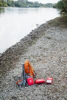 On the beach, adjacent to a flowing river, there is a backpack resting alongside some first aid kits, indicating readiness for adventure and exploration in the great outdoors photo
