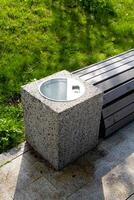 There is a trash can placed conveniently next to a rustic wooden bench in a lovely park, creating a practical spot for visitors to sit and enjoy the surroundings without littering photo