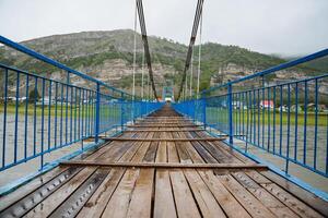 A serene landscape featuring a wooden bridge with a blue railing crossing over a calm body of water, circled by trees under a clear sky. A peaceful scene for leisure and relaxation photo