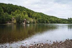 The tranquil river setting, surrounded by a forest and rocky shore, offers a serene and picturesque view of natures beauty, ideal for finding peace and tranquility photo