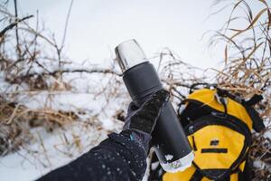 A person tightly grips a thermos while standing amid the snow, ensuring that its warm contents maintain a comfortable temperature despite the frigid and freezing environment around them photo
