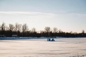 A beautiful and serene snowy field, with tall trees standing in the background and a bright blue tent prominently placed in the foreground, creating a stunning winter scene photo