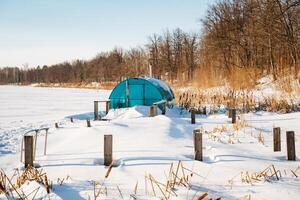 A bright blue tent is prominently situated right in the center of a vast, snowy field that stretches endlessly in all directions, capturing the essence of a winter wonderland photo