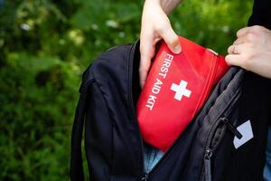A person is carefully placing a first aid kit into their backpack while preparing for an upcoming journey or travel event, ensuring they are equipped for any potential emergencies photo
