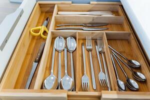 A kitchen drawer is wellorganized with cutlery and utensils in a wooden divider, creating an efficient storage solution. The setup showcases a clever and neat arrangement photo