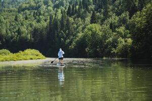 Experience inner peace while paddleboarding along a serene river, surrounded by lush forests, and connecting with nature to enjoy tranquility in a peaceful environment photo
