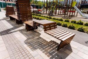 Wooden benches in the park create a serene atmosphere with a playground in the background, offering a tranquil setting for visitors to relax and enjoy nature while surrounded by greenery photo