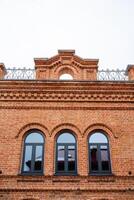 In the neighborhood stands a stunning brick building featuring three elegant arched windows, each with a charming balcony above, showcasing exquisite architectural details photo