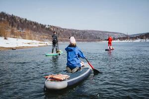 SUP boarding on the river, a man rowing with a paddle sitting on an inflatable board, spring rafting of a group of people on a lake in nature. photo
