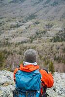 Traveler with a backpack sits on a rock admiring the valley landscape photo