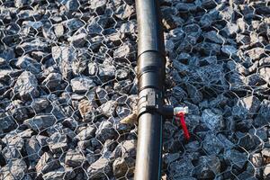 A sturdy black pipe featuring a bright red valve is positioned on top of an uneven pile of rocks, creating an interesting contrast between the industrial and natural elements around it photo