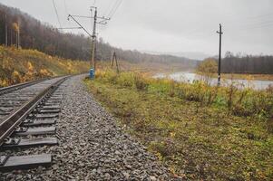Train track cuts through field with river, trees, and clouds in background photo