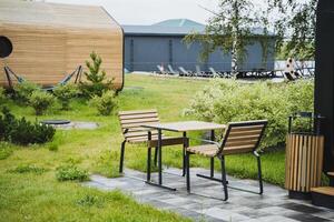 Visualize a contemporary outdoor patio furnished with wooden pieces, including a hammock, set in a tranquil park, ideal for relaxation and connecting with the beauty of nature photo
