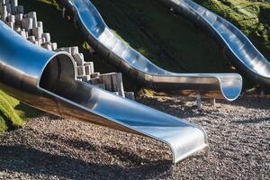 In a lovely park, there exists a delightful row of shiny stainless steel slides, providing endless fun and excitement for children while enjoying the lovely surroundings in leisure time photo