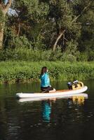 A woman peacefully relaxes on a paddleboard in a tranquil moment, drifting on calm waters, embraced by natures beauty and tranquility of the natural landscape around her photo