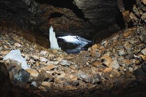 There exists a fascinating cave that features a stunning, large ice sculpture positioned right in the center of it, surrounded by natural beauty. Its presence captivates all who enter photo