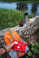 A tourist first aid kit against the background of a backpack for a hike, equipment for tourism, a thermos with tea, a walk in the forest in the summer. photo