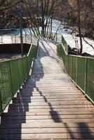A charming wooden bridge featuring a green fence gracefully leads to a serene river, enhancing the natural beauty of the landscape with its inviting pathway and picturesque surroundings photo
