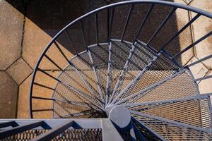 Aerial view of a beautifully designed spiral staircase with a mesh design and textured ground surface beneath photo