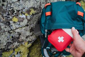 Hand taking out first aid kit from hiking backpack, red first aid kit on a journey, concept of an autonomous hike in the forest. photo
