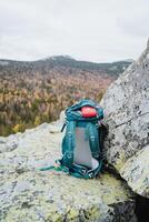 A tourist backpack stands on a rock against the background of the mountains, equipment for hiking in the mountains, a red first aid kit is in the pocket of the bag. photo