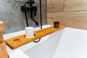 Discover the Elegant Bamboo Bathtub Tray, complete with a soothing candle and cup designed for your ultimate relaxation experience photo