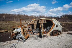 The open doors of a car burned down after a crash on the road, the car is standing in a field against the background of a blue sky. photo