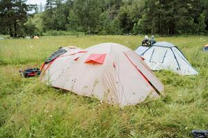 In a tranquil wilderness field, camping tents are set amidst lush greenery and trees, providing a peaceful setting for outdoor enthusiasts to relax and enjoy nature photo