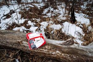 A first aid kit is positioned on a log that rests in the snow, showcasing the stark contrast between the warm colors of the kit and the cold, white landscape surrounding it photo