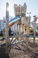A delightful wooden playground featuring a colorful slide right in the center, surrounded by trees and grass, creating a fun space for children to play and enjoy their time outdoors photo