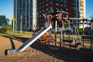 A colorful slide found in a playground accompanied by a tall building situated in the background, enhancing the urban landscape and showing a blend of leisure and residential areas photo