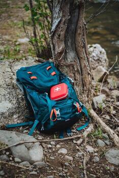 Adventure backpack with first aid kit leaning against tree by riverside in the wilderness. Essential gear for outdoor exploration, safety, and emergency preparedness photo