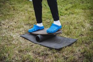 In the image, a person wearing electric blue crocs stands on a board, surrounded by grass and trees, in a recreational setup. Includes keywords like plant, tree, grass, recreation photo