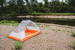 Experience the tranquility of camping by a peaceful river, with a tent pitched on the rocky bank in a lush forest ideal for relaxing and connecting with nature photo