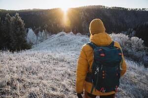 Man with backpack traveling in the mountains in winter view from the back, trekking in the mountains at dawn of the day, hiking in nature in December, glare of the sun over the mountain. photo
