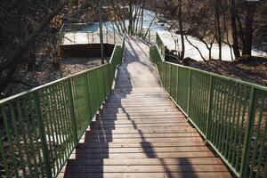 A beautifully scenic wooden footbridge gracefully stretches over a serene, calm river, surrounded by vibrant nature in the soft morning light, offering a perfect escape for all photo