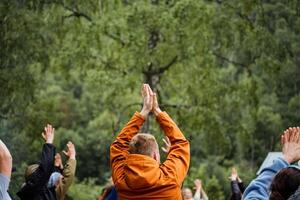 A group of people are standing in a circle with their hands in the air enjoying the natural landscape. They seem to be having a leisurely and recreational time in the forest during an event photo