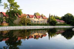 A beautiful house featuring striking red roofs stands proudly alongside a tranquil lake, where its charming image is mirrored perfectly in the calm waters, creating a picturesque view photo