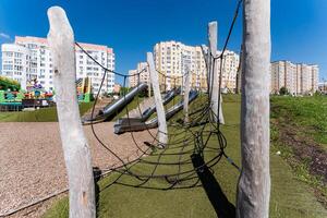 The playground features a slide and a rope bridge, offering kids an engaging and enjoyable play space within an urban environment infused with natural elements like greenery photo