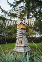 In a beautiful park filled with vibrant greenery, a charming wooden windmill stands proudly in the grass, surrounded by a picturesque natural landscape under the clear blue sky photo