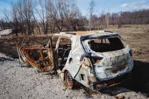 The car after the accident is in an open field outside the city, a burnt car, a rusty piece of metal, a disaster on the road. photo