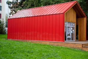 A striking red building that features a wellconstructed wooden frame along with a matching red roof is prominently located on top of a lush, vibrant green field that surrounds it photo