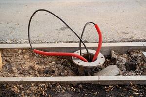 An exposed electrical junction box displaying red and black wires located on an urban sidewalk, posing a hazard photo