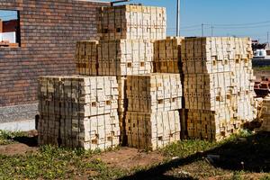 The neatly stacked wooden pallets at a construction site by a brick building under a clear sky symbolize progress in the infrastructure sector and efficient materials management photo
