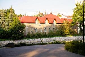 The charming house features a vibrant red roof and is surrounded by lush trees and colorful bushes that enhance its beauty and blend it harmoniously into the natural landscape around it photo