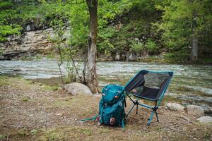 Backpack and chair resting by river in natural landscape photo