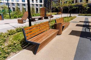A scene of a modern urban park with benches and walkways in bright summer daytime, surrounded by buildings, greenery, and nature, ideal for relaxation and recreation photo