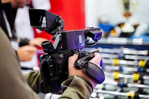 A man is currently holding a camera securely in his hands right in front of a foosball table, ready to capture the exciting action or fun moments taking place there photo